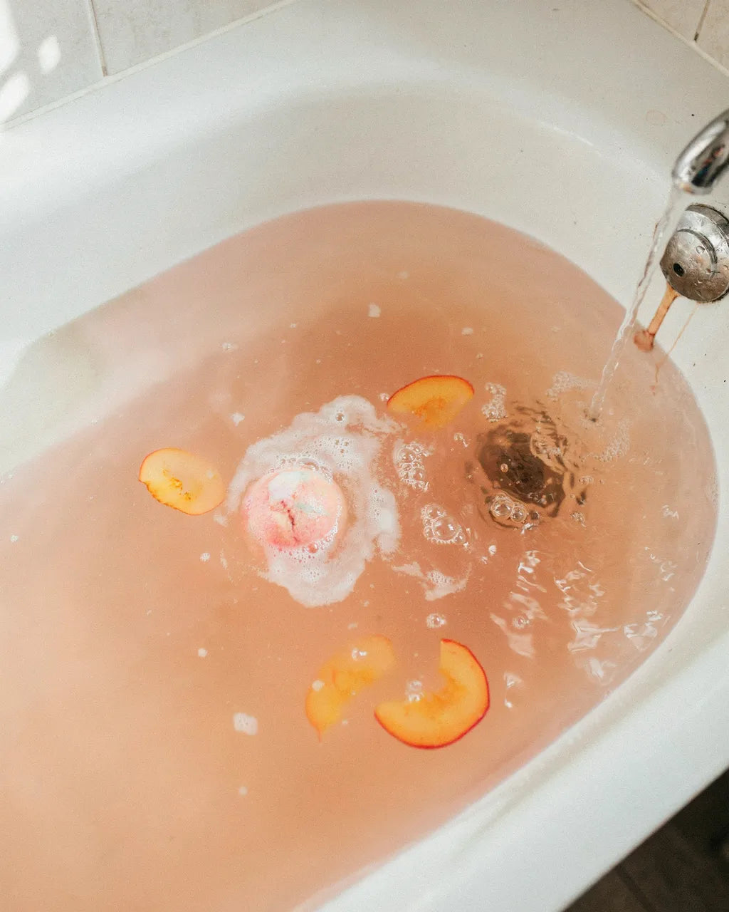 Creamy Peach Rush bath bomb turning the bath blush-peach with peach slices