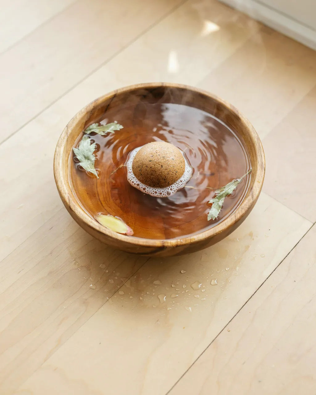 Eight-Herb mugwort foot-soak ball fizzing in a wooden basin of warm herbal water